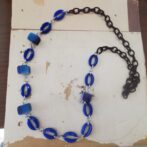 Blue circular bead necklace with silver links arranged on a light wooden surface.